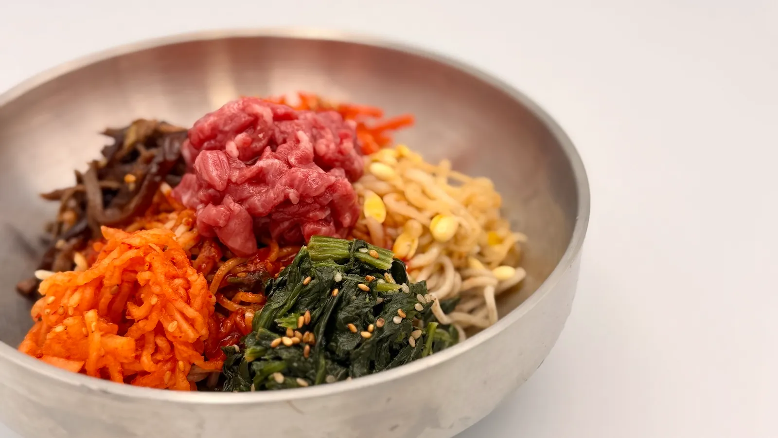 甘辛いコチュジャンだれとナムルを混ぜ合わせる冷たい混ぜそば「ピビンマックッス」を器に盛った様子